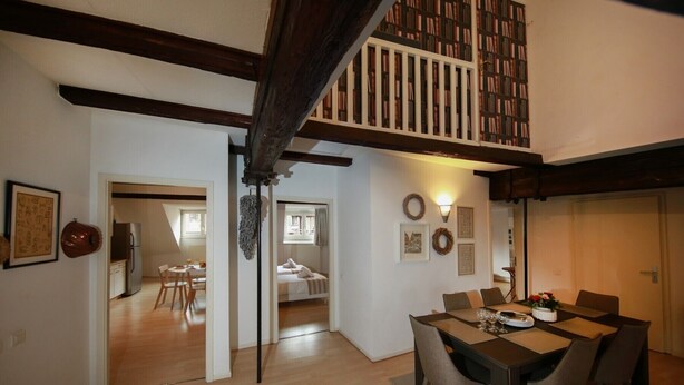 Una habitación amplia con techo alto, una zona de comedor con mesa y sillas, y un rincón acogedor con cama.
