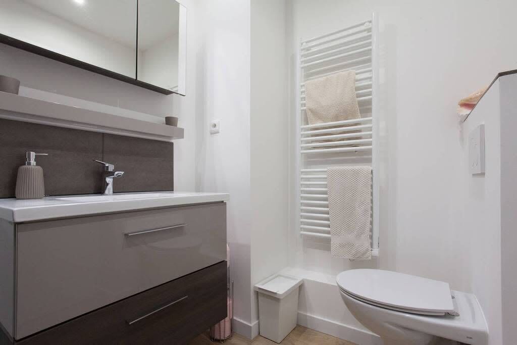 Une salle de bain moderne avec un lavabo blanc, un miroir et des toilettes. On y trouve un porte-serviettes sur lequel est accrochée une serviette.