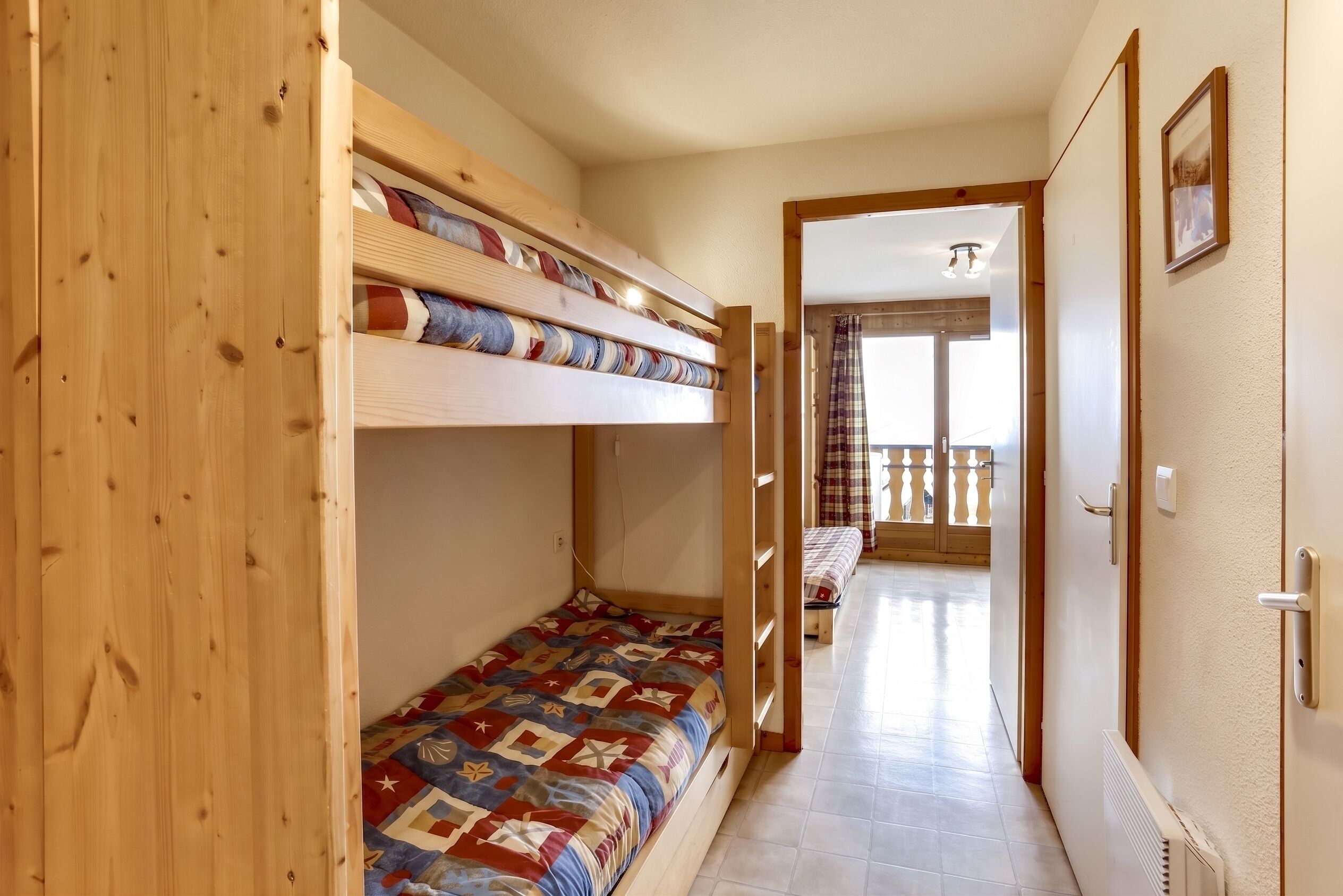 Habitació amb lliteres, una porta de fusta, un passadís que condueix a una altra habitació i vista a un balcó.