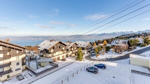 Un barrio residencial con edificios de varios pisos, una calle cubierta de nieve y una vista de montañas distantes.