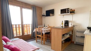Una habitación con cama, escritorio, silla, televisión y zona de cocina.