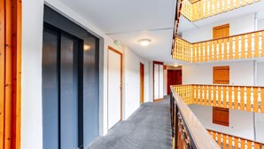 Un pasillo de hotel con alfombra gris, barandilla de madera y una escalera que lleva a un balcón de madera.