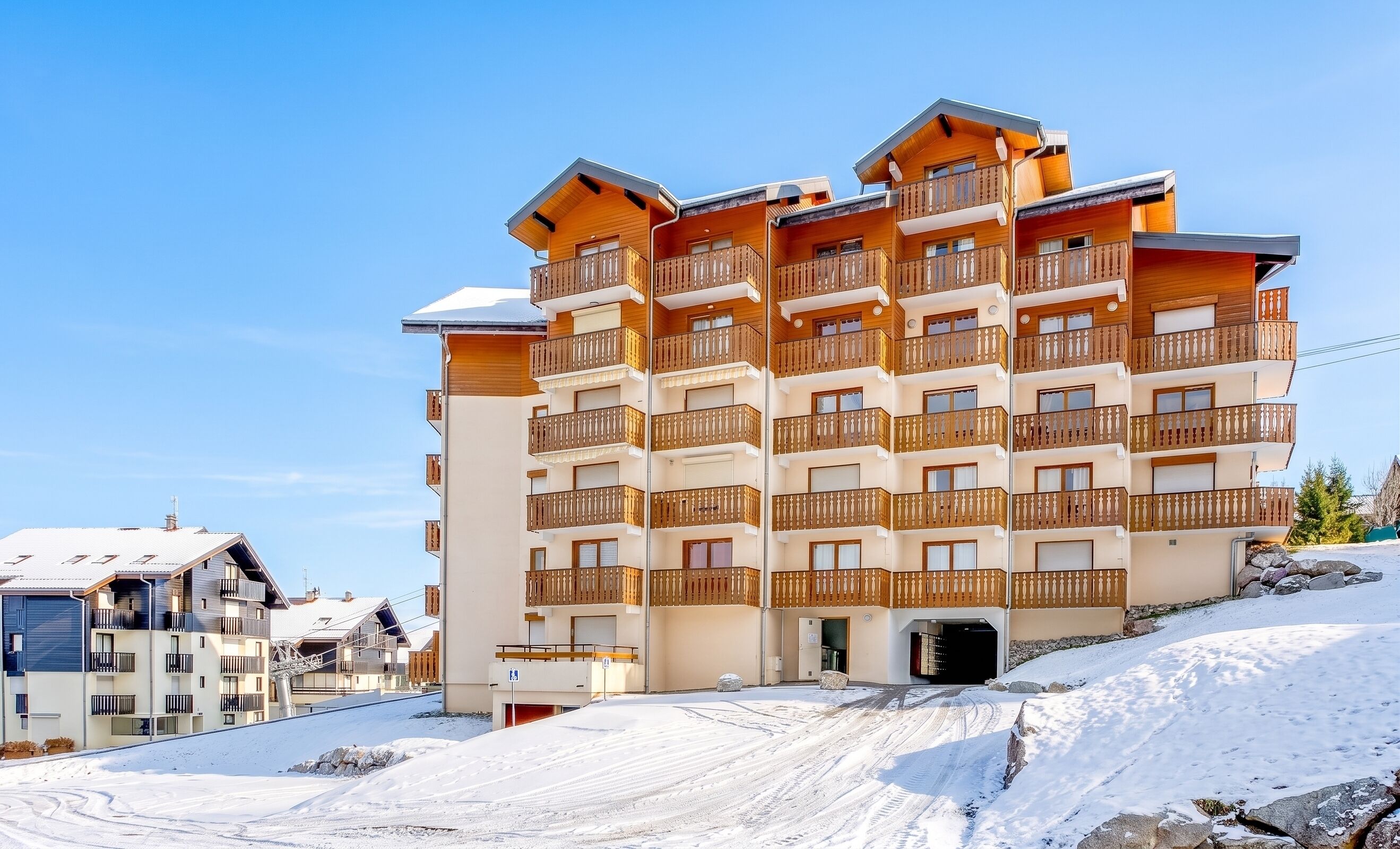 Un hôtel à plusieurs étages doté de balcons, avec une piste de ski en arrière-plan et un ciel dégagé.