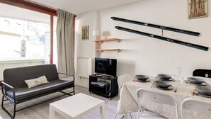 Una sala de estar moderna con un sofá, una mesa de comedor con cuencos, un televisor y equipo de esquí en la pared.