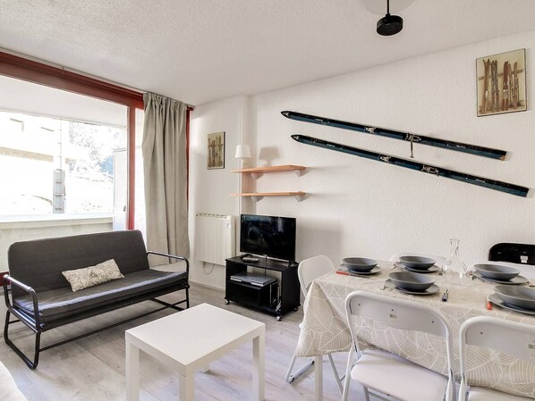 Un salon moderne avec un canapé, une table à manger dressée avec des bols, un téléviseur et du matériel de ski accroché au mur.
