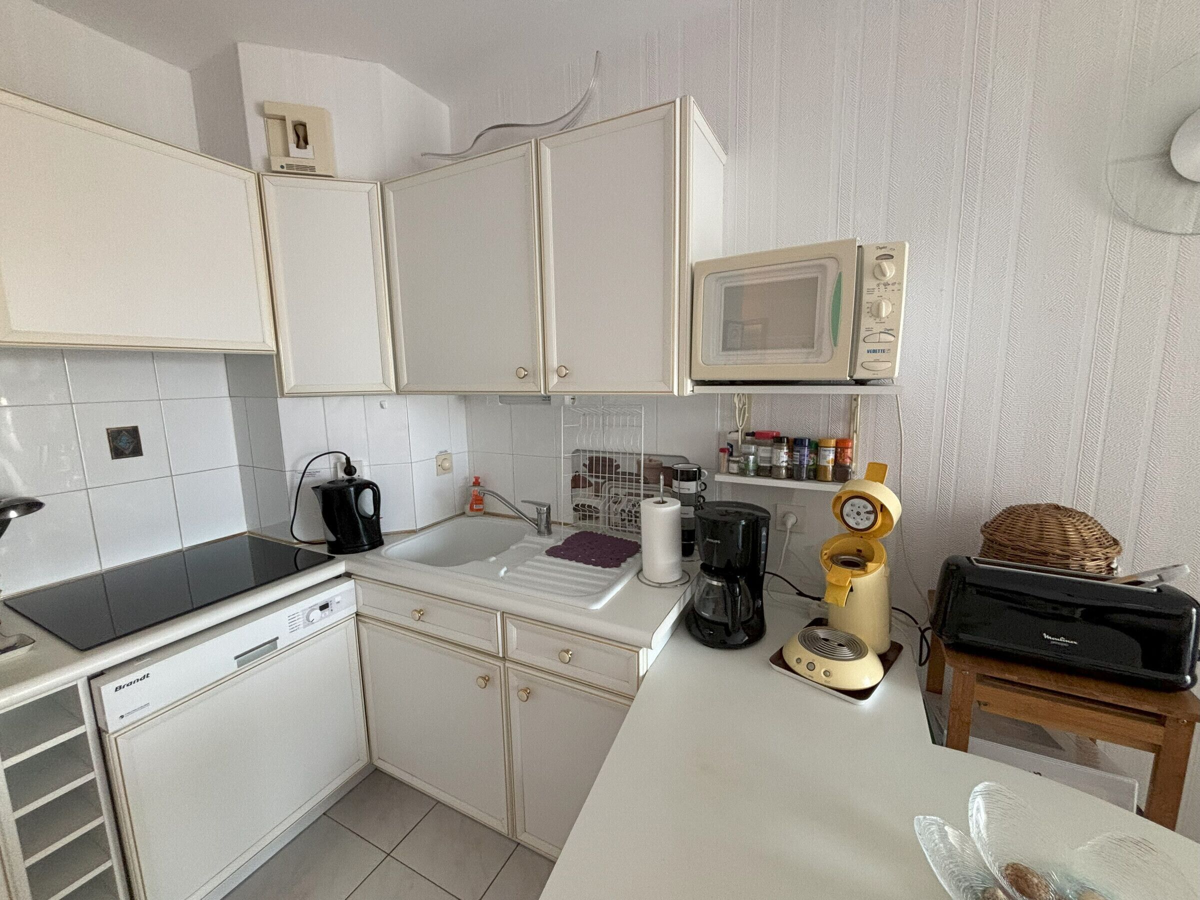A compact kitchen with white cabinets, a microwave, a coffee maker, and a toaster.