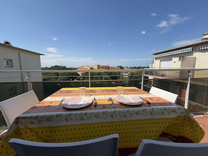A balcony with a table set for two, overlooking a cityscape.