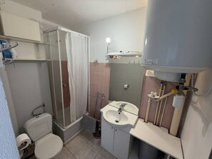 A compact bathroom with a toilet, shower, sink, and a mirror above the sink.