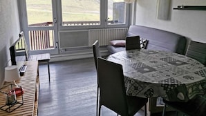 A cozy room with a large window, a sofa, a table with a patterned tablecloth, and a chair. - Ski-in/Ski-out Apartment for 6 with Balcony, South-Facing, 1 Bedroom, La Mongie (La Mongie)