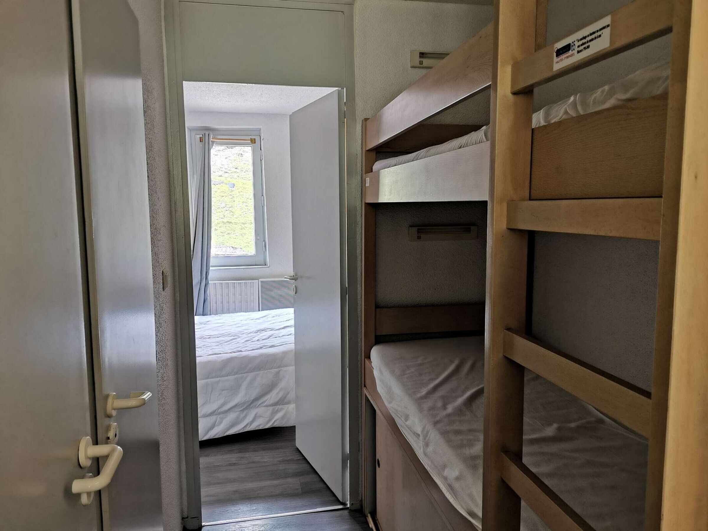 Ein schmaler Flur mit einem Etagenbett auf der rechten Seite und einem Einzelbett in einem Zimmer am Ende.
