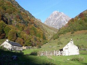 A rural landscape with two stone buildings, one with a gabled roof and another with a simple design, surrounded by lush greenery and a mountain in the background. - Ski-in/Ski-out Apartment for 6 with Balcony, South-Facing, 1 Bedroom, La Mongie (La Mongie)