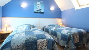 Een slaapkamer met twee bedden, blauwe wanden, een poster van een schip en een dakraam.