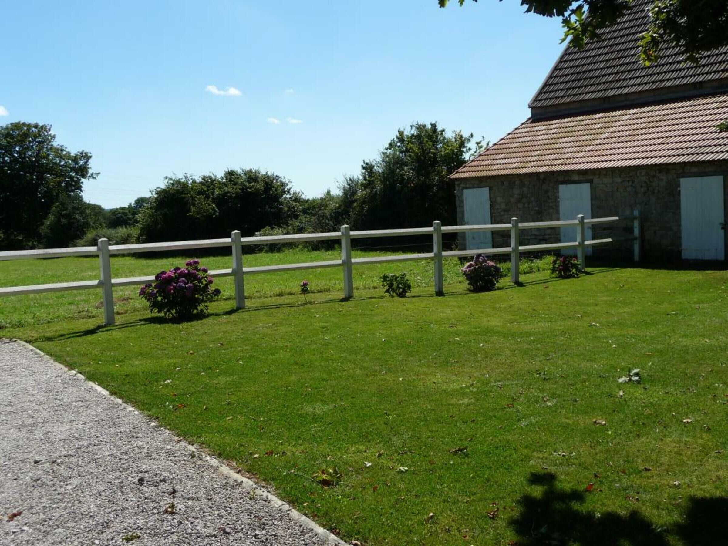 A grassy area with a white fence, a stone building with a tiled roof, and a gravel path.