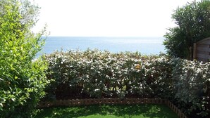 Un jardin avec une clôture en bois, de l’herbe verte et une vue sur la mer.