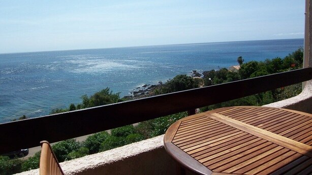 Un balcon avec une table en bois et une vue sur l’océan.