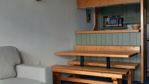 Een kleine leefruimte met een stapelbed, een kitchenette en een zithoek met bankjes.
