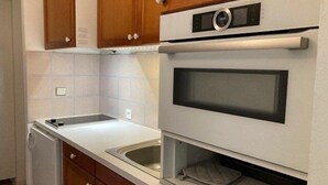Une cuisine de taille réduite, dotée de meubles de rangement en bois, d’un four encastré et d’un évier.
