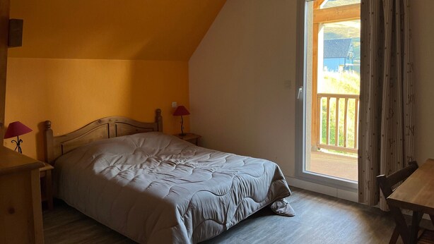 Ein Schlafzimmer mit Bett, Nachttisch, Lampe und Blick ins Freie durch ein Fenster.