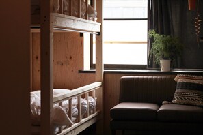 A room with a bunk bed, a cushioned bench, a potted plant, and a window with curtains. - glam lodge - Hostel (Osaka)
