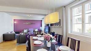 A dining area with a table set for four, a sofa, a TV, and a purple wall. - schlumberger 120m2 city center 3br 2bth (Colmar)