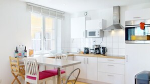 A modern kitchen with white cabinets, a microwave, an oven, and a dining area with a table and chairs. - schlumberger 120m2 city center 3br 2bth (Colmar)