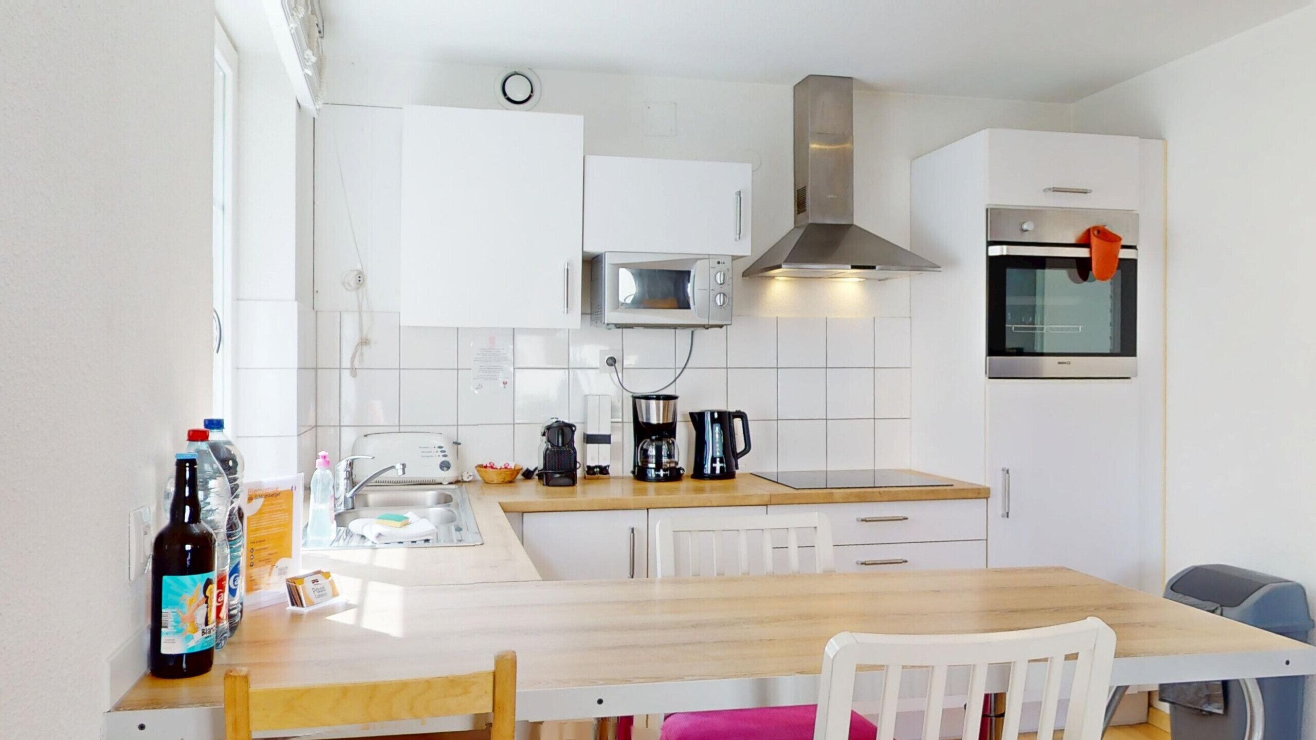 A compact kitchen with a microwave, stove, and sink. There is a dining table with chairs and a small window.