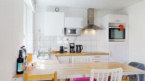 Eine kleine Küche mit Mikrowelle, Herd und Spüle. Ein Esstisch mit Stühlen und ein kleines Fenster sind vorhanden.