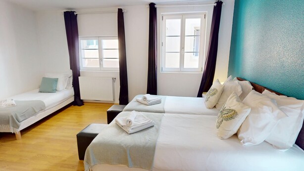 A hotel room with two single beds, a double bed, a wooden floor, and a window with curtains. - schlumberger 120m2 city center 3br 2bth (Colmar)