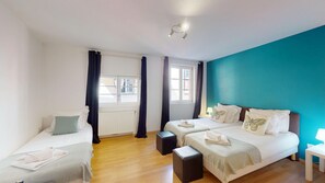 Ein Zimmer mit zwei Betten, einem Fenster, einer Heizung und einer Wand in Türkis.