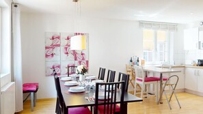 A dining area with a table set for four, chairs, a wall with floral artwork, and a kitchen area with a window.