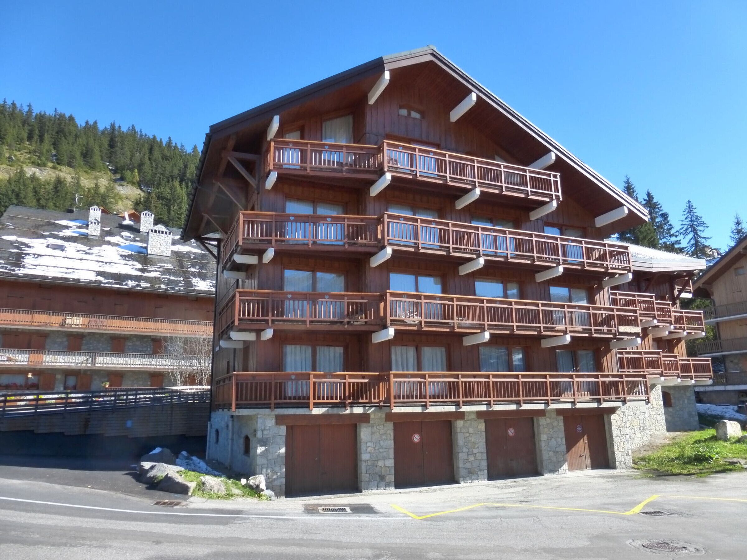 Un immeuble en bois à plusieurs étages, doté de balcons et de murs en pierre, avec une piste de ski en arrière-plan.