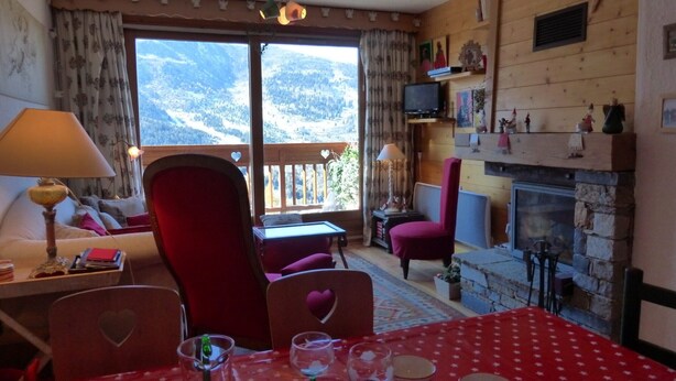 Un'accogliente stanza con camino, un tavolo apparecchiato per mangiare, una televisione e vista sulle montagne dalla finestra.