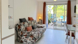 A living room with a patterned sofa, a ceiling fan, and a sliding glass door leading to an outdoor area with a table and chairs.