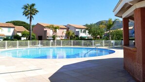 A swimming pool with a white fence, surrounded by buildings with red-tiled roofs and palm trees.