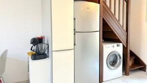 A compact kitchen with a built-in refrigerator, a washing machine, and a coffee maker.