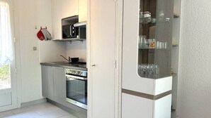A compact kitchen with a microwave, oven, and a glass cabinet with dishes.