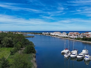 Un port de plaisance où sont amarrés plusieurs bateaux, un ciel bleu dégagé et des bâtiments qui bordent la rive.