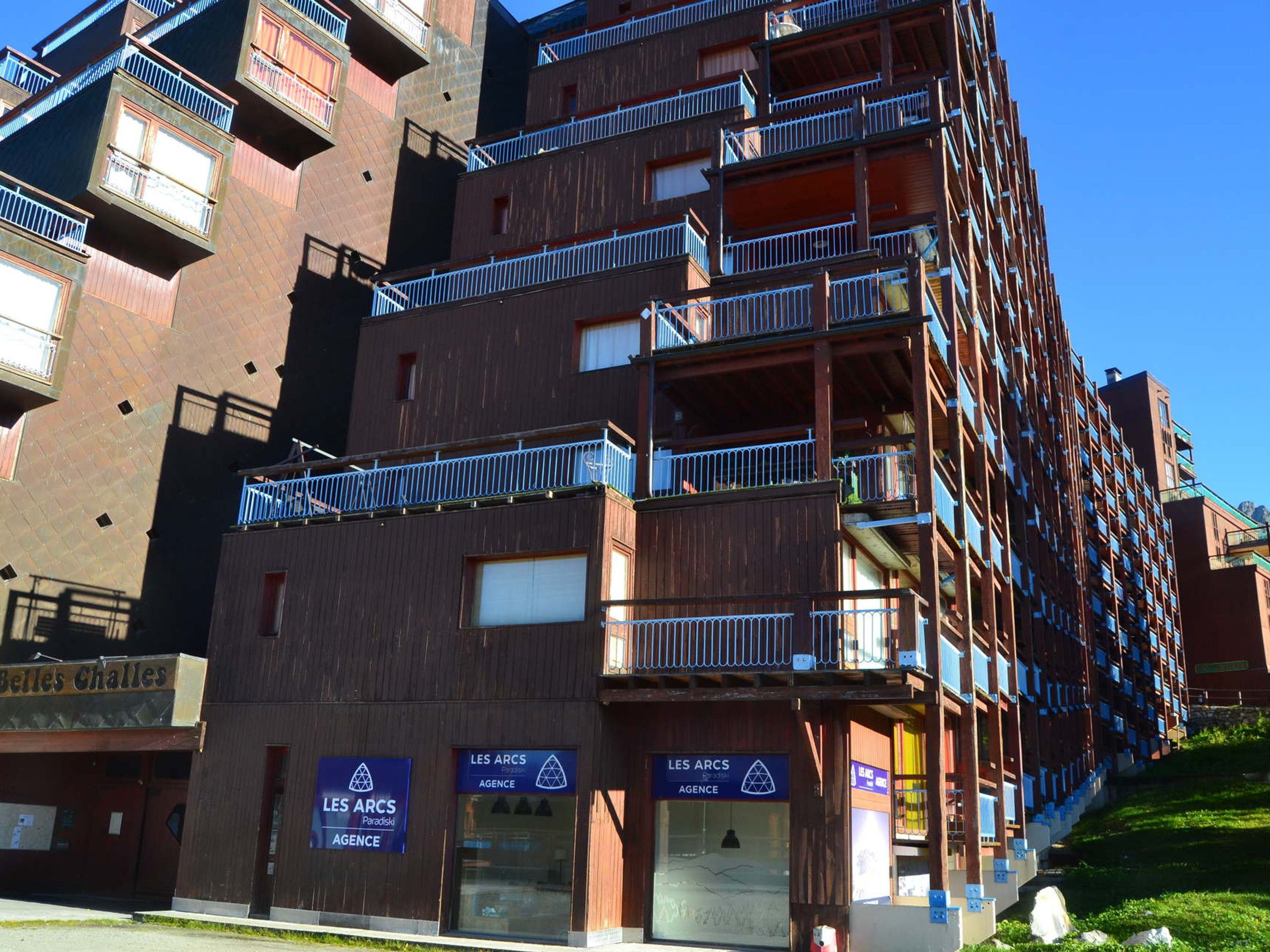 A multi-story building with balconies, signs for 'LES ARCS AGENCY' and 'Belles Challes', and a visible entrance.
