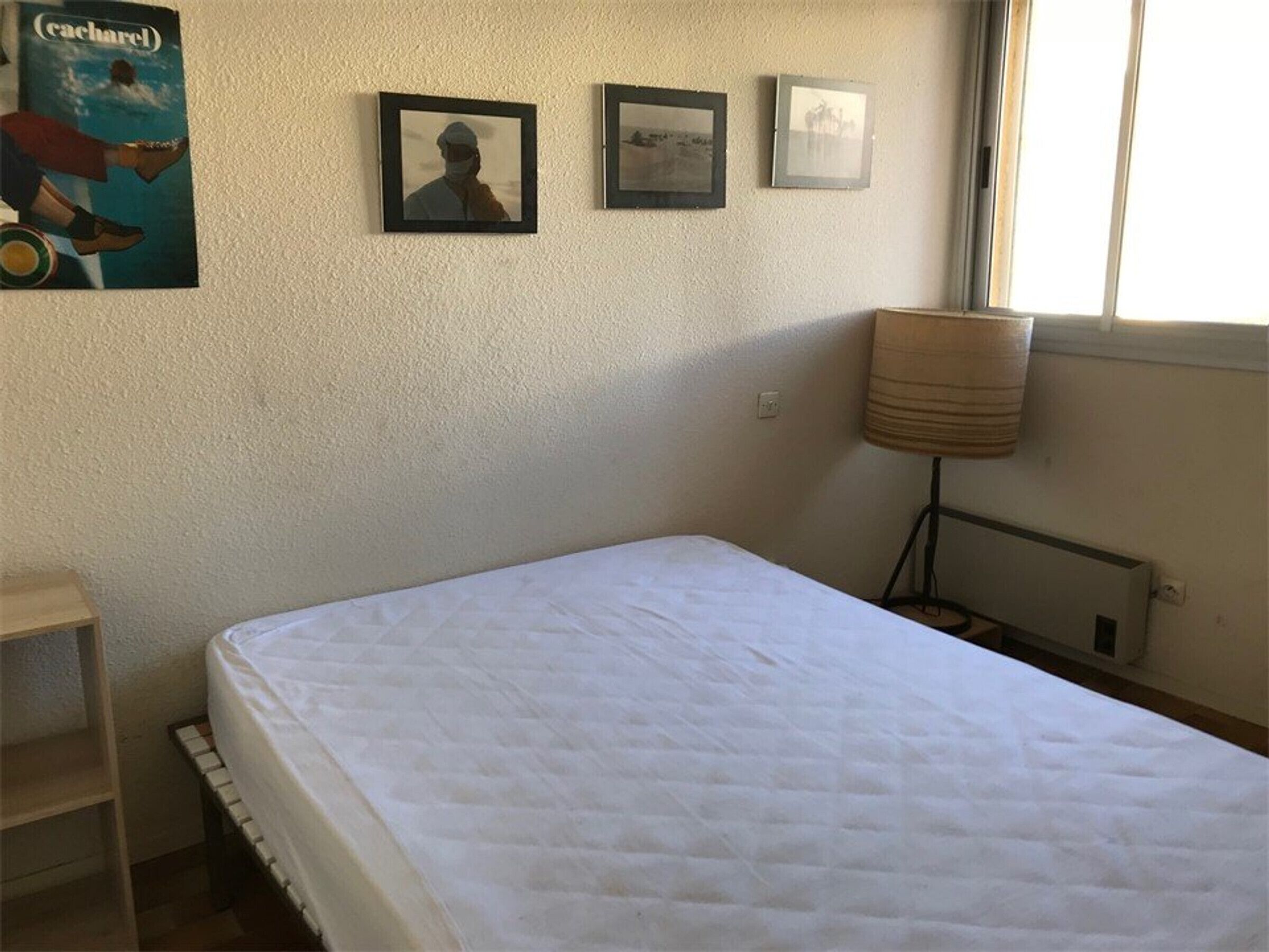 A bedroom with a single bed, a window, and three framed pictures on the wall.