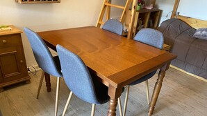 Una mesa de comedor de madera con cuatro sillas, un armario de madera y una cama al fondo.