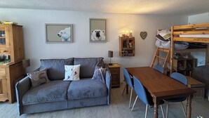 Una sala de estar acogedora con un sofá gris, una mesa de comedor de madera y una cama litera.
