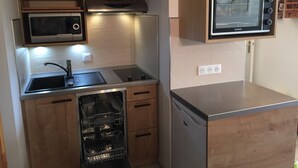 Cocina compacta con armarios de madera, microondas integrado, lavavajillas y horno pequeño.