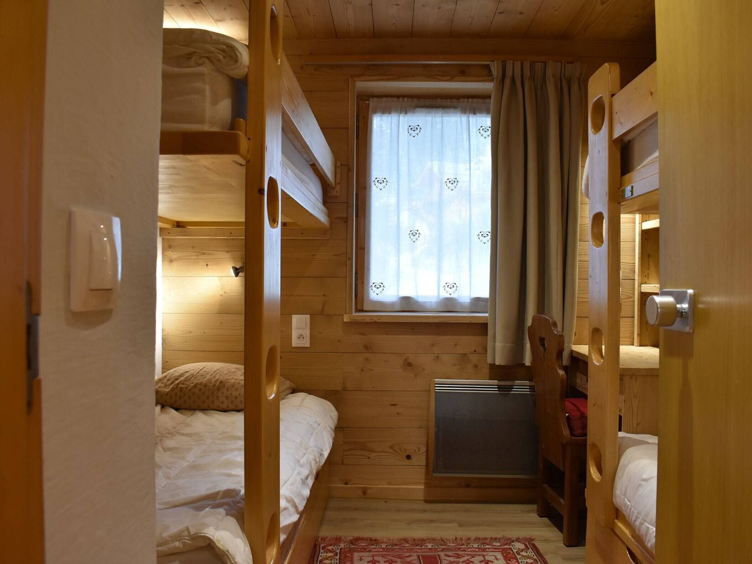 A compact wooden cabin room with bunk beds, a small window with curtains, and a heater.