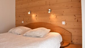 A wooden-paneled room with a bed, two wall-mounted lights, and a small wooden bench. - Ski-In/Ski-Out Apartment with Fireplace and Balcony in Méribel (Méribel)