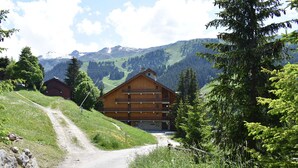 A wooden chalet with a balcony, surrounded by lush greenery and mountains in the background. - Ski-In/Ski-Out Apartment with Fireplace and Balcony in Méribel (Méribel)
