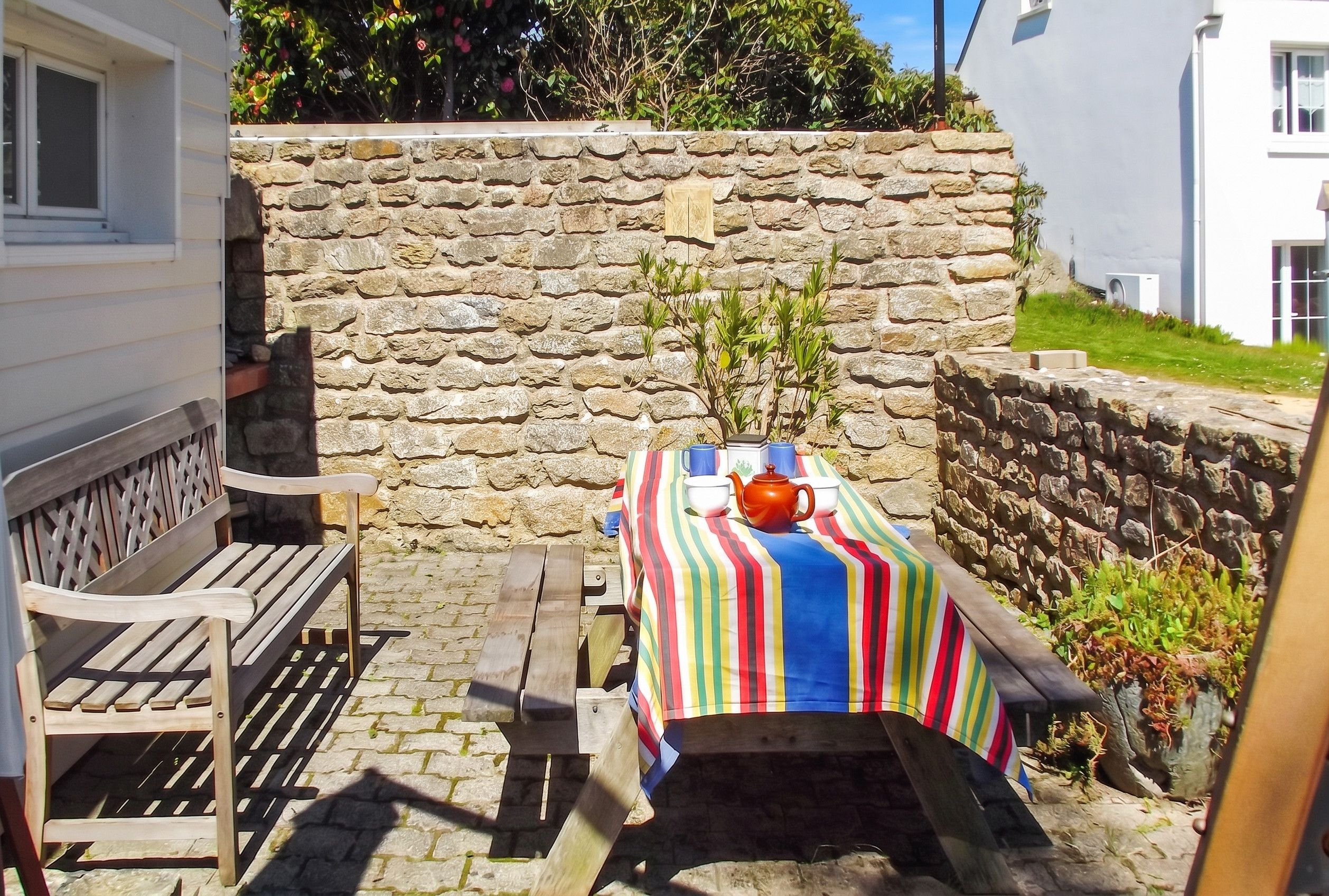 Un mur de pierres avec une table dressée pour le thé, un banc et une petite plante.