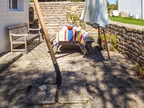 A stone wall, a wooden bench, a table with a striped tablecloth, and a white umbrella. - Homerez - Charming House in Trédrez-Locquémeau + Garden (Trédrez-Locquémeau)