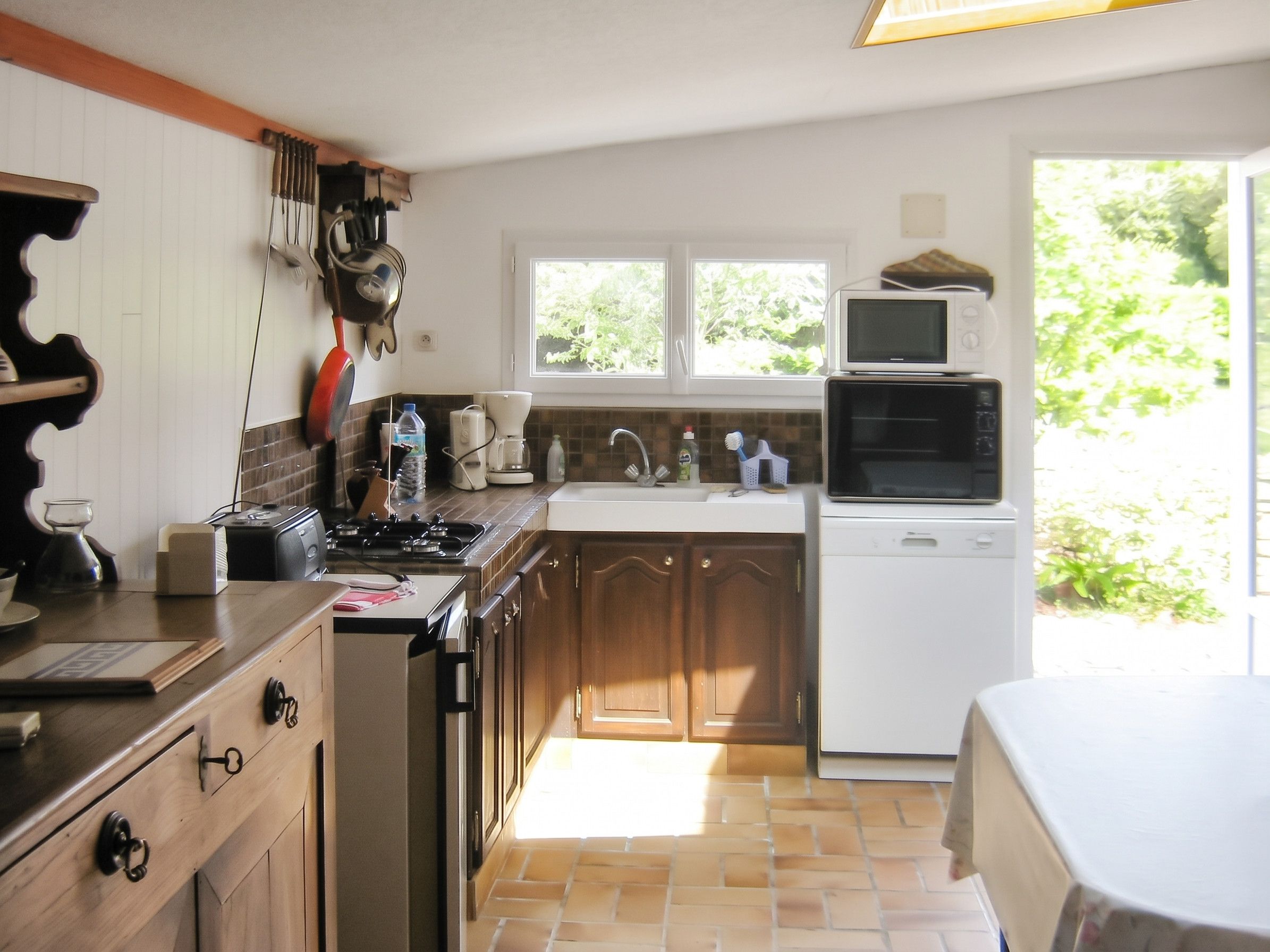 A kitchen with a stove, sink, and a microwave. There are cabinets and a window with a view of greenery outside.