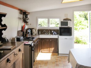 A kitchen with a stove, sink, and a microwave. There are cabinets and a window with a view of greenery outside.
