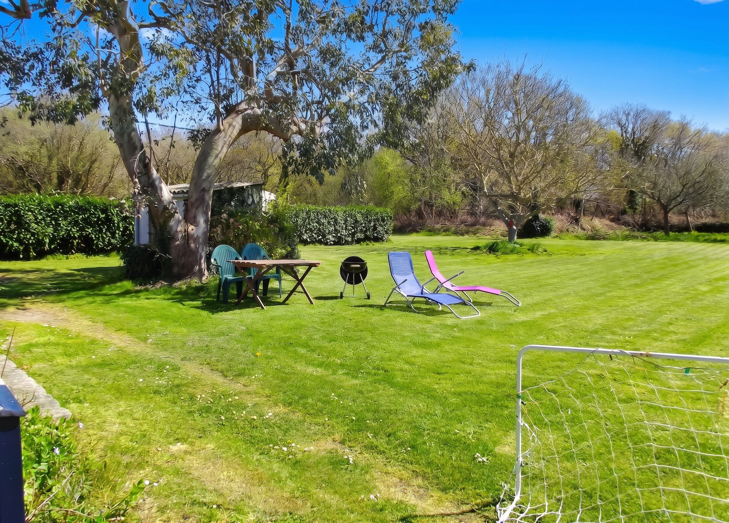 Un espacio al aire libre con césped, una mesa y sillas, una parrilla y un arco de fútbol.